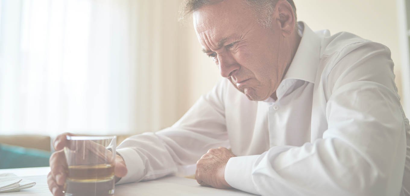 Мужчина пьет алкоголь сидя за столом